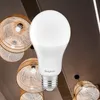 A white LED light bulb is shown in the foreground, with decorative woven lampshades in the background. Produktbild-Vorschau