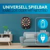 A dartboard is mounted on a blue wall, with a sofa and a cabinet visible in the foreground. Icons indicating battery and plug power options are displayed. Produktbild-Vorschau