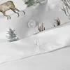 A close-up view of a white duvet cover with a watercolor print of a winter forest scene, featuring a deer, trees, and grass. A white button is visible. Produktbild-Vorschau
