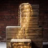 A cascade of warm white fairy lights spills over stacked wooden crates against a brick wall. Produktbild-Vorschau