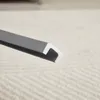 A close-up view of a gray and white U-shaped profile strip, likely a furniture edge or seal, resting on a textured light gray and white carpet. Anteprima dell’immagine prodotto