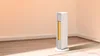 A white and gold electric heater stands in the corner of a room with light peach walls and a wooden floor. Voir les images du produit