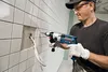 A man is using a Bosch hammer drill to drill a hole in a tiled wall, with wires coming out of the hole. Anteprima dell’immagine prodotto
