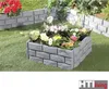 A garden planter box made of gray, brick-patterned material, filled with colorful flowers, set on a lawn. Produktbild-Vorschau