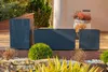 Three dark gray concrete planters of different sizes are arranged on a patio with decorative stones and plants in the foreground and background. Produktbild-Vorschau