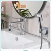 A chrome bidet sprayer set attached to a white sink faucet, with a round mirror and plants in the background. Náhľad obrázku produktu