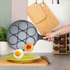 A hand is holding a non-stick frying pan with 7 circular molds, over a plate with a fried egg and a pancake with a strawberry. The scene is set in a kitchen with cutting boards and spice racks in the background. Anteprima dell’immagine prodotto