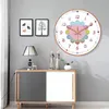 A wall clock is displayed on a wall above a cabinet, with two framed pictures and a lamp on the cabinet. Produktbild-Vorschau