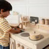 A young boy is playing with a wooden toy kitchen. Anteprima dell’immagine prodotto