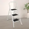A white 3-step folding step stool is shown in a room with a light-colored wall and wooden floor. Produktbild-Vorschau