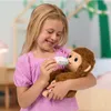 A young girl feeding a toy monkey with a bottle in a bedroom. Podgląd zdjęcia produktu