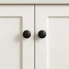A close-up view of two black cabinet knobs on white cabinet doors. Produktbild-Vorschau