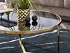 A close-up of a round coffee table with a black marble top and gold trim, featuring a gold vase with a plant and two black decorative balls. Náhled obrázku produktu