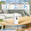 A white smart thermometer/humidity sensor is placed on a wooden coffee table in a living room setting. The background shows a blurred sofa and cushions. Produktbild-Vorschau