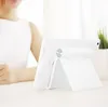 A person in a white top is sitting at a table with a white tablet stand. Náhľad obrázku produktu