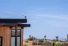 A Starlink Mini internet kit is mounted on the roof of a modern wooden house in a desert landscape. Produktbild-Vorschau