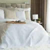 A neatly made bed with a white quilted bedspread, decorative pillows, and a throw blanket. Náhľad obrázku produktu