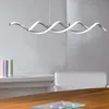 A modern LED pendant light fixture with a twisted design, shown hanging above a desk in a well-lit room. Produktbild-Vorschau