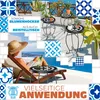 A woman relaxing on a lounge chair on a balcony overlooking the sea, with mosaic tables and plants around her. Produktbild-Vorschau