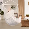A white hammock chair is hanging in a living room with plants and curtains in the background. Náhled obrázku produktu