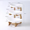 A three-tiered fruit and snack stand with white ceramic bowls and a natural wood base. Náhled obrázku produktu