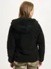 A woman wearing a black fleece jacket and camouflage pants, viewed from the back. Produktbild-Vorschau