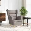 A taupe fabric armchair is shown in a well-lit room with a wooden dresser and a plant. Náhľad obrázku produktu