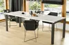 A modern dining room with a white high-gloss extendable dining table and black chairs, set against a backdrop of large windows overlooking a garden.