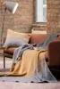 A cozy living room scene with a sofa, throw blanket, pillow, and floor lamp. Produktbild-Vorschau