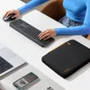 A person's hands are shown using a laptop, keyboard, and mouse on a white desk. A laptop sleeve and a smartphone are also visible. Anteprima dell’immagine prodotto