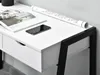 A close-up view of a white desk with black metal legs, featuring a magazine, a smartphone, and a rolled-up document. Voir les images du produit