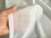 A hand holding a sheer white fabric with vertical stripes. Produktbild-Vorschau