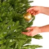 Hands decorating a Christmas tree with a gold ornament. Produktbild-Vorschau