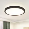 A modern, circular LED ceiling light with a black frame and a white diffuser, mounted on a white ceiling. The background shows a hint of a room with green curtains and a white wall. Náhľad obrázku produktu