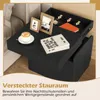 A black nightstand with a coffee cup, books, and picture frames on top. The top surface is partially open, revealing a storage compartment with an orange book and a watch. Text in German and Russian is present. Podgląd zdjęcia produktu