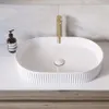 A white oval countertop sink with a gold faucet and a bottle of soap on a white countertop. Anteprima dell’immagine prodotto
