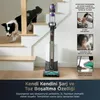 A dog is walking down stairs next to a vacuum cleaner. The vacuum cleaner is in a charging station. Anteprima dell’immagine prodotto