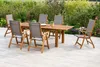 A wooden dining set with chairs on a patio surrounded by greenery. Náhled obrázku produktu