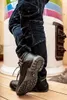 A person wearing work boots and jeans stands in front of a colorful tiled stove. Náhled obrázku produktu