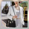 A woman in a white suit walks down a city street, holding a black handbag. Produktbild-Vorschau