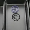 A close-up view of a stainless steel kitchen sink with a drain and a clear plastic lid. Náhled obrázku produktu