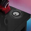 A close-up view of a black gaming desk with a carbon fiber texture, featuring a silver cable grommet and a red headphone stand with headphones on it. Náhled obrázku produktu