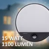 A close-up of a black LED outdoor wall light with a motion sensor, set against a blurred background of a house at dusk. Text overlays provide product specifications. Produktbild-Vorschau