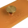 A close-up of an orange pot lid with a brass knob and embossed text. Produktbild-Vorschau