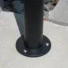 Close-up of the base of a black metal pole mounted on a concrete surface. Produktbild-Vorschau