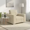 A cream-colored armchair is placed on a fluffy white rug in a well-lit room. A small side table with a plant and a cup is next to the armchair. A floor lamp and a painting on the wall are also visible. Náhľad obrázku produktu