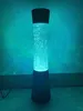 A tall, cylindrical lamp with a black base and top, filled with glowing blue bubbles. Anteprima dell’immagine prodotto