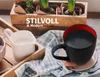 A breakfast setting with a cup of coffee, a creamer, and plants in the background. Produktbild-Vorschau