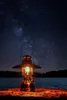 A lantern sits on a wooden surface by a lake under a starry night sky. Náhľad obrázku produktu