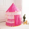A pink princess castle play tent is shown in a room with a white wall and floor. A small cactus in a pot and a wooden toy are also visible. Náhled obrázku produktu